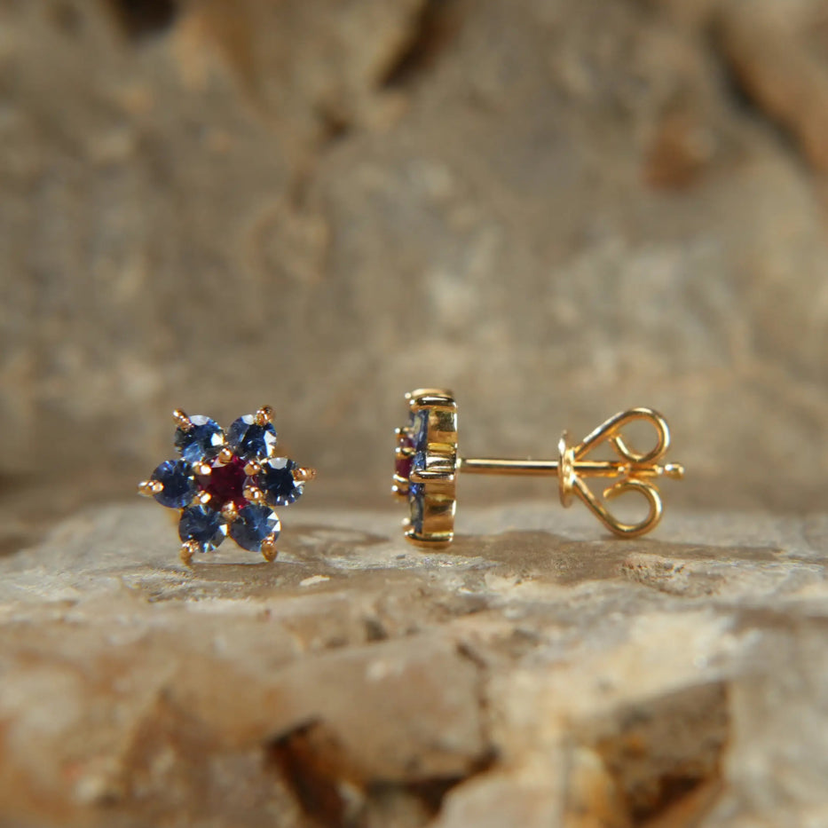 Gold stud earrings with blue sapphires and central ruby on stone background, Eclat d'or jewelry