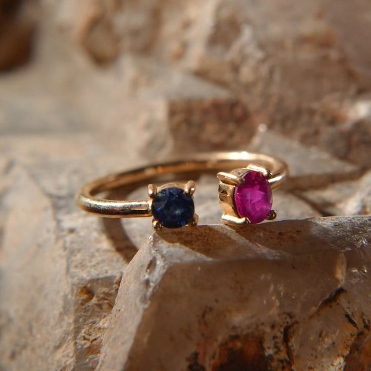 Gold ring with sapphire and ruby gemstones, luxury jewelry from Eclat d'or on stone background.
