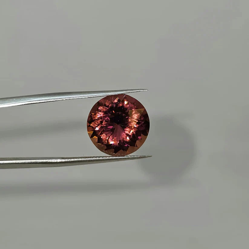 Round cut pink rubellite tourmaline gemstone held by tweezers, luxury jewelry stone
