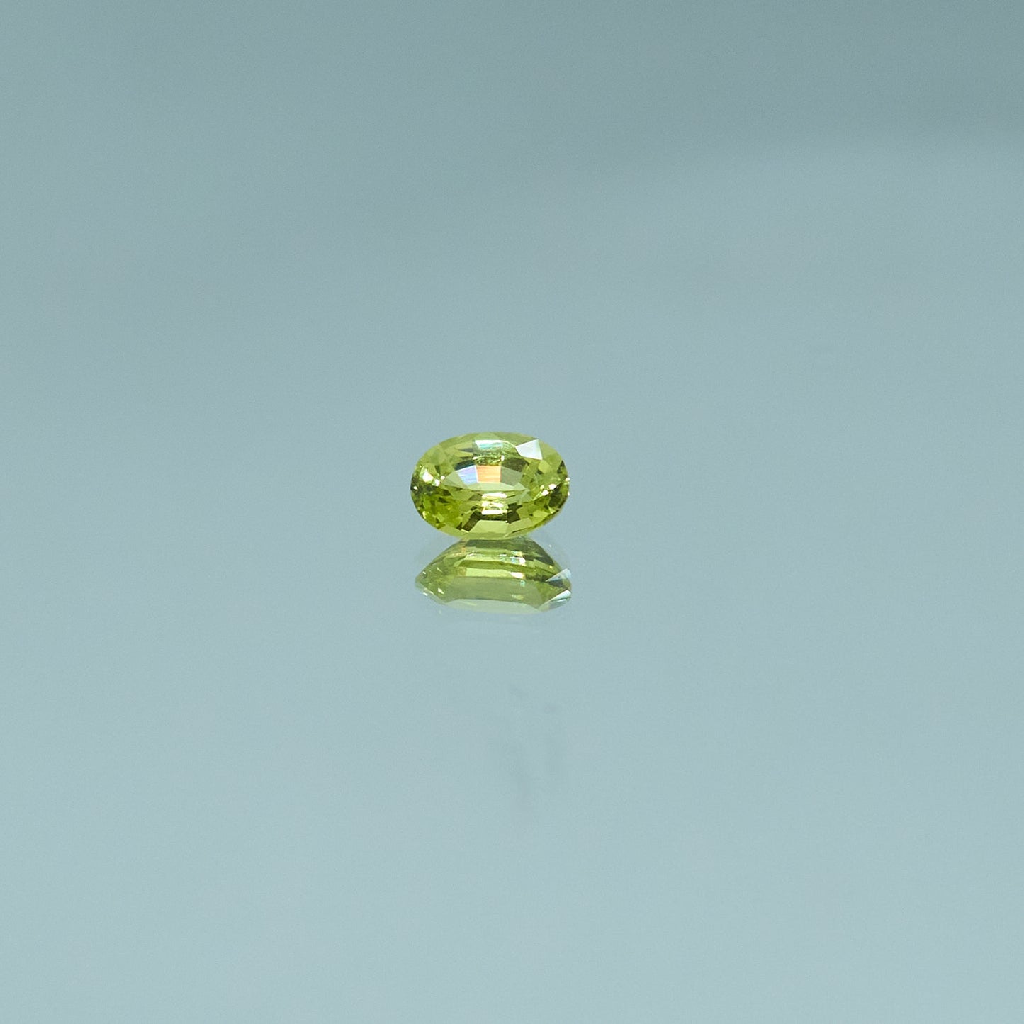 Oval-cut green chrysoberyl gemstone reflecting on a glossy surface for Eclat d'or jewelry