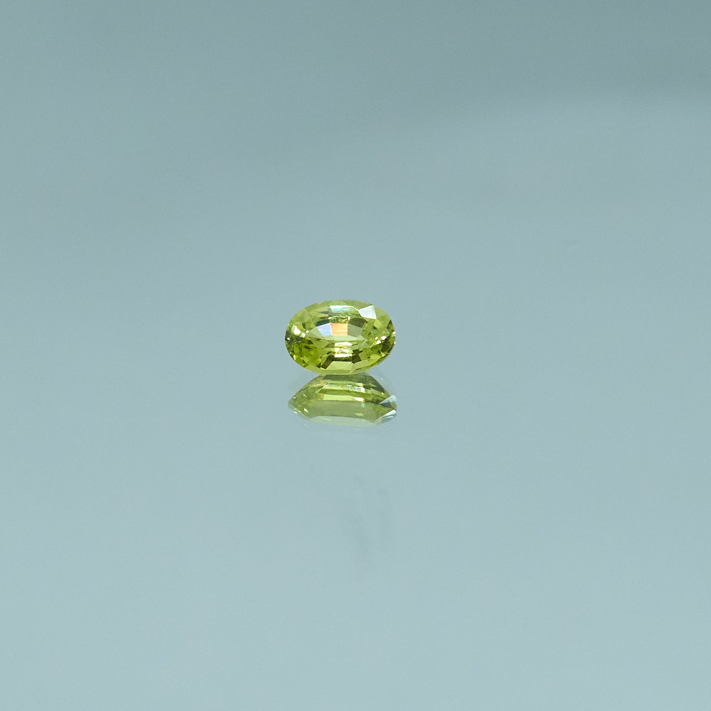 Oval-cut green chrysoberyl gemstone reflecting on a glossy surface for Eclat d'or jewelry