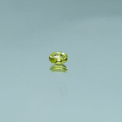 Oval-cut green chrysoberyl gemstone reflecting on a glossy surface for Eclat d'or jewelry